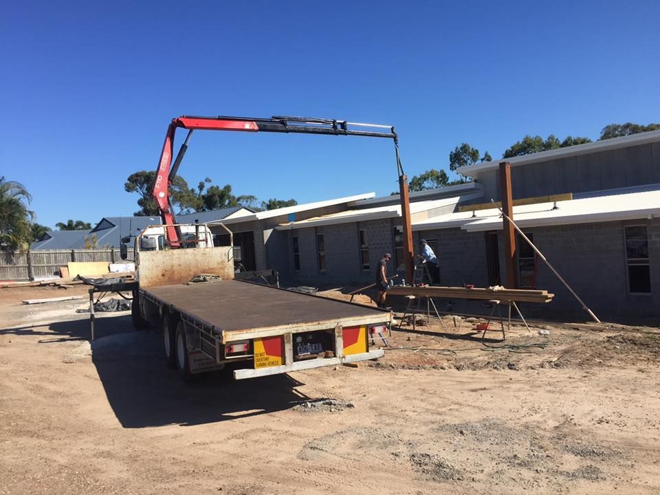 A Truck with A Crane Is Lifting Wooden Beams at A Construction Site — J & M Transport Plus in Rockhampton, QLD
