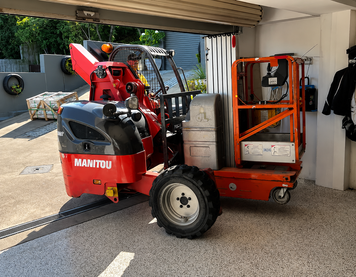 Red MANTOU construction lift parked in a garage beside a wall and open doorway.