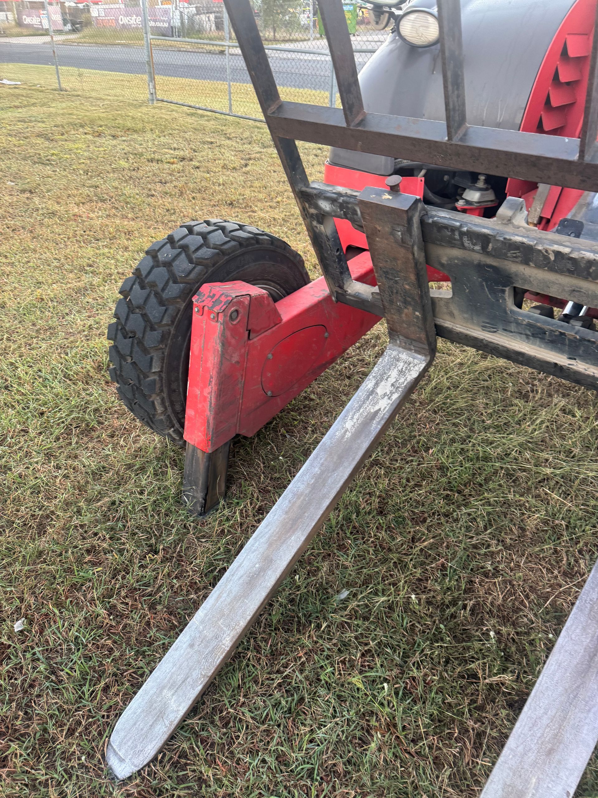 Red metal trailer jack with black wheel and silver support bars on grass.