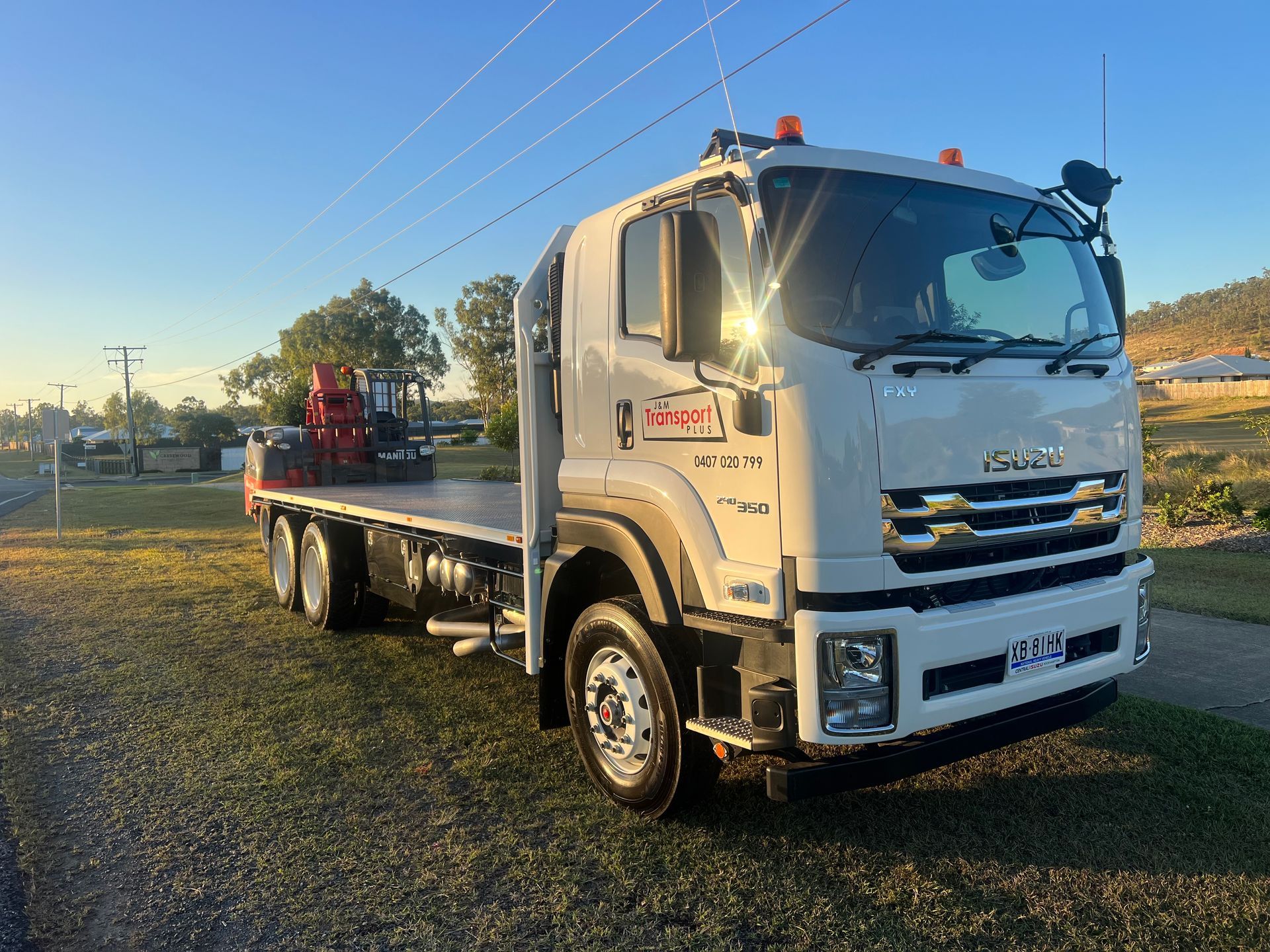 White flatbed tow truck parked on grass at sunset, with power lines and trees in the background