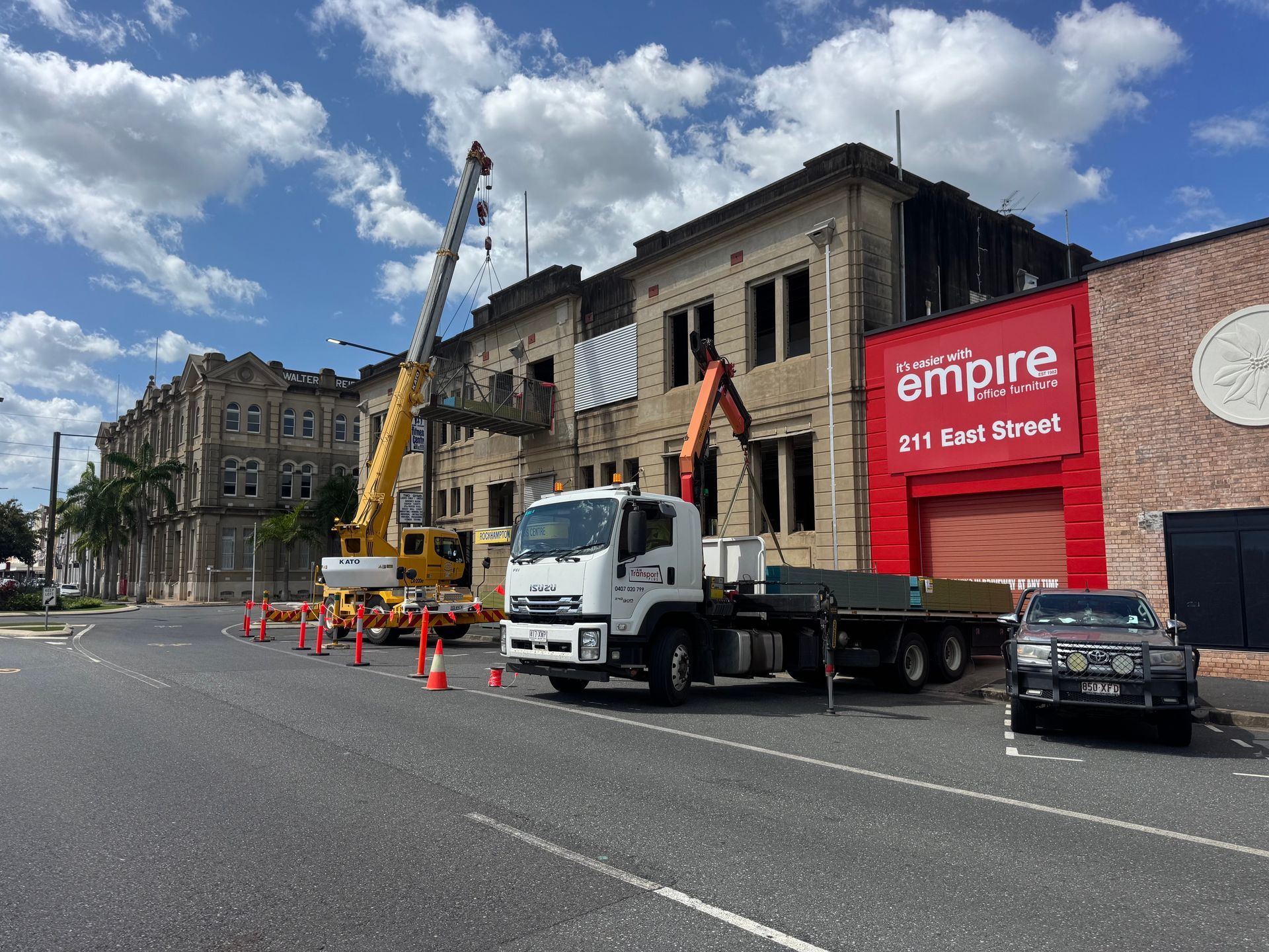 Truck and crane beside a damaged building, with cones and an Empire sign under a cloudy sky