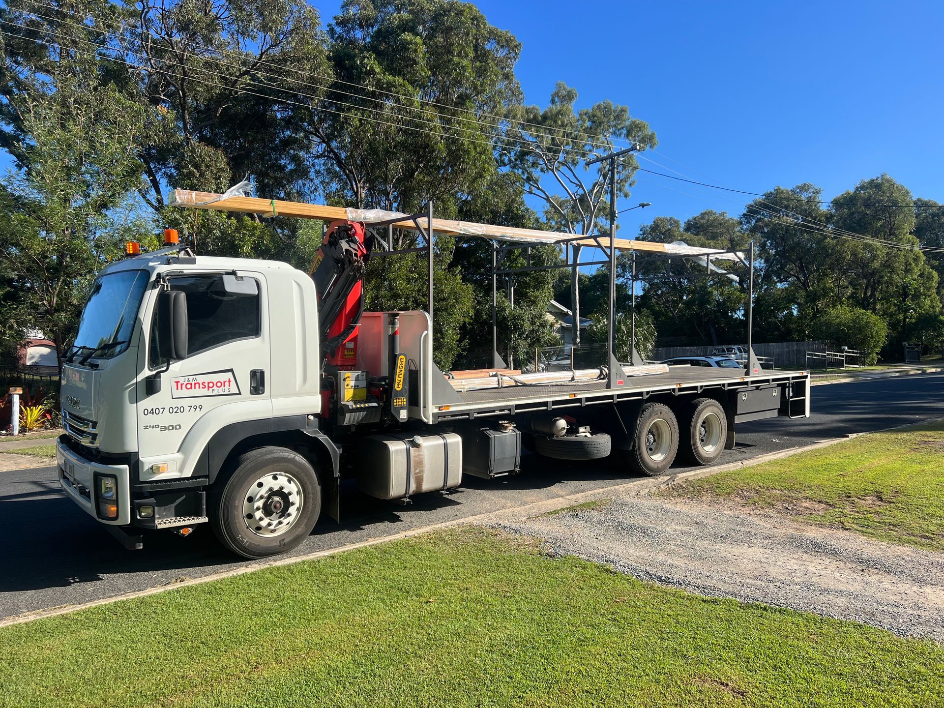 White flatbed tow truck parked on a roadside beside grass and trees under a clear blue sky
