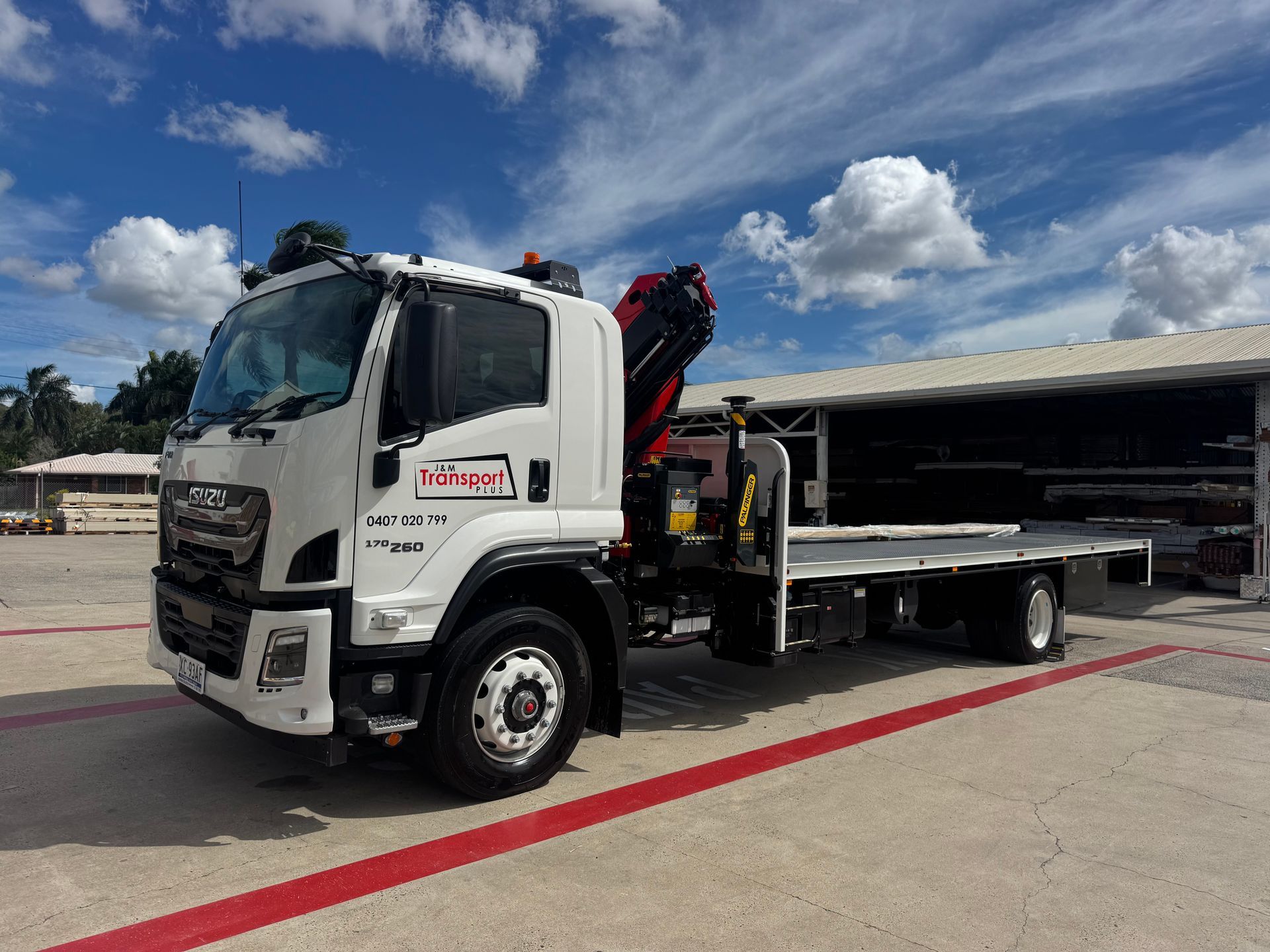 White flatbed tow truck parked outside a building under a blue sky with clouds