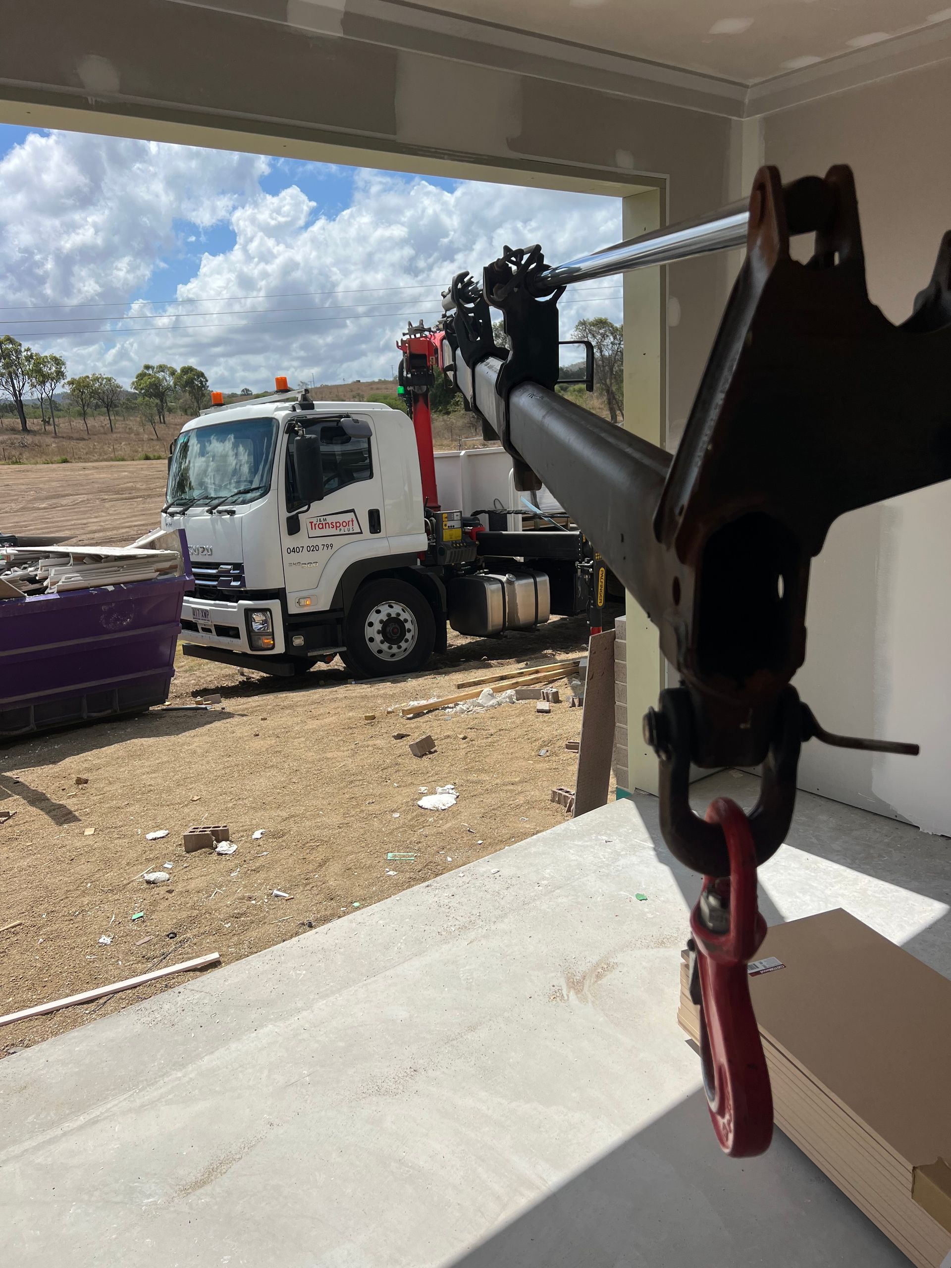 Truck with crane arm lifting debris outside a building, seen from a shaded porch.