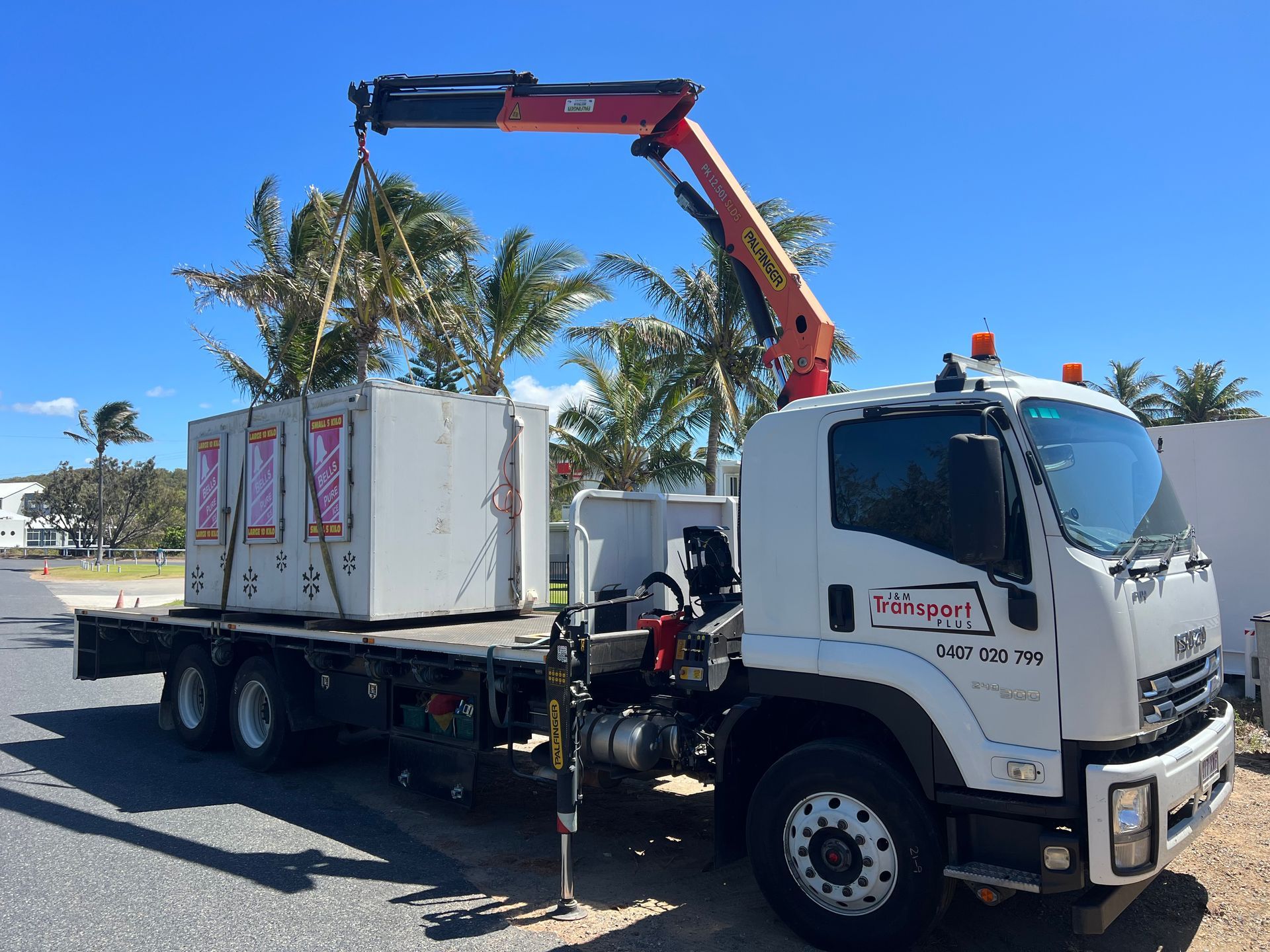Tow truck loading a white shipping container with a crane arm on a sunny street