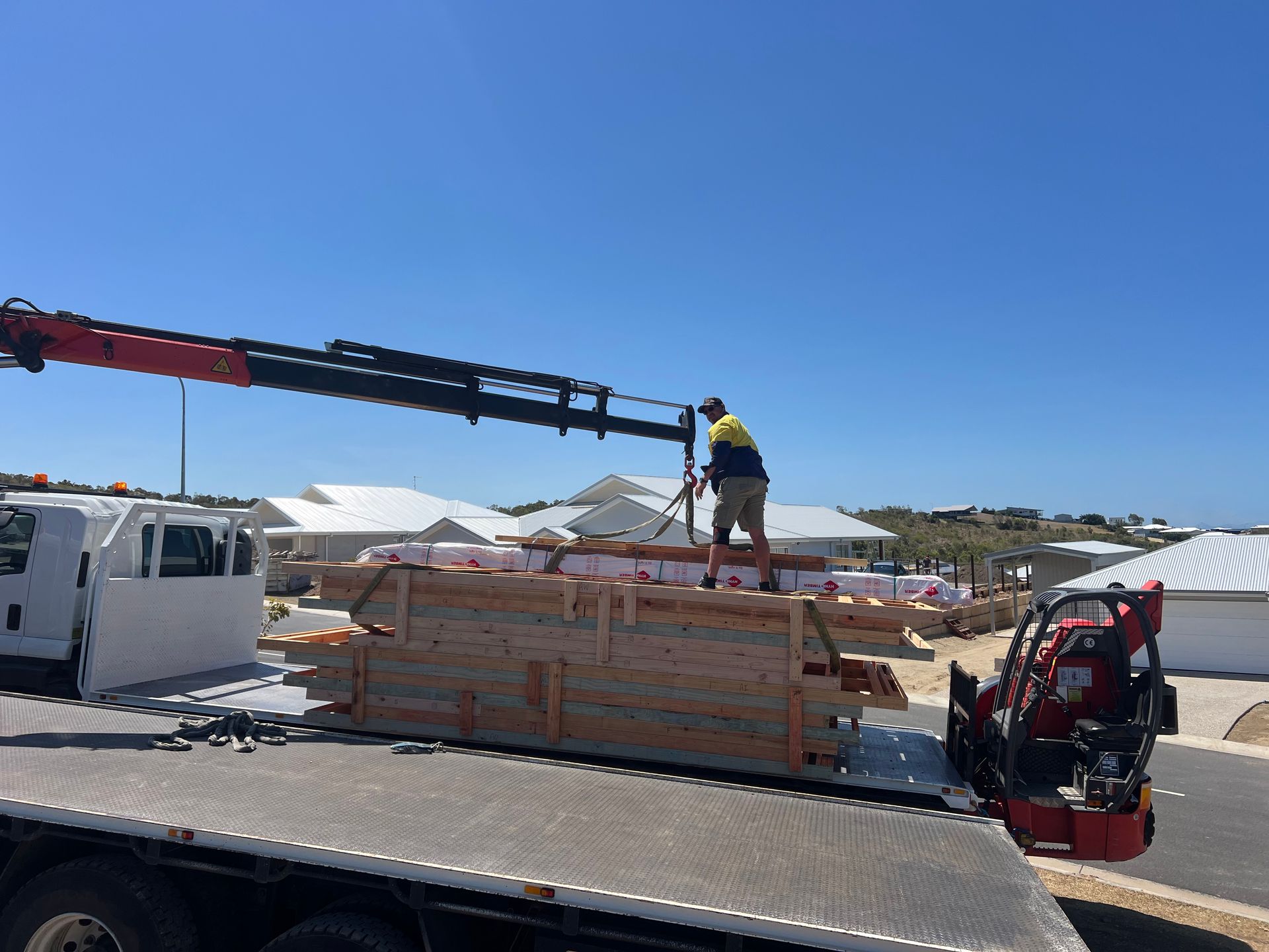 Construction worker on stacked lumber using a crane in a sunny outdoor worksite
