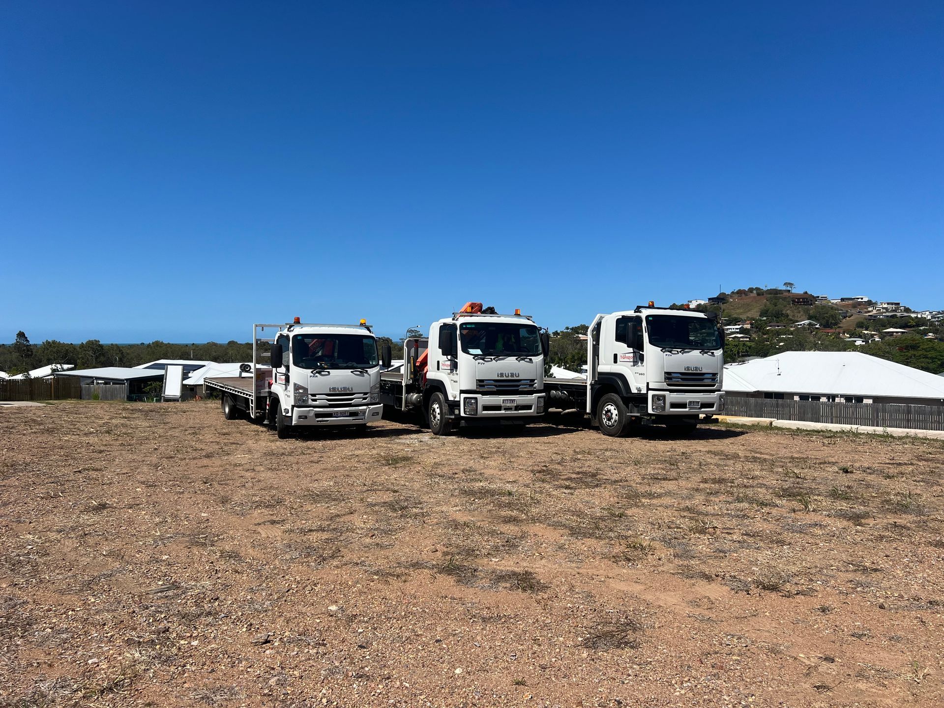Three white trucks parked on a rocky lot under a clear blue sky