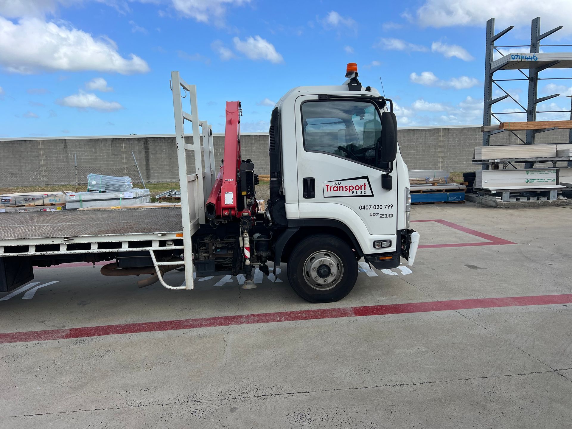 White flatbed truck with red crane parked on an outdoor lot under a blue sky