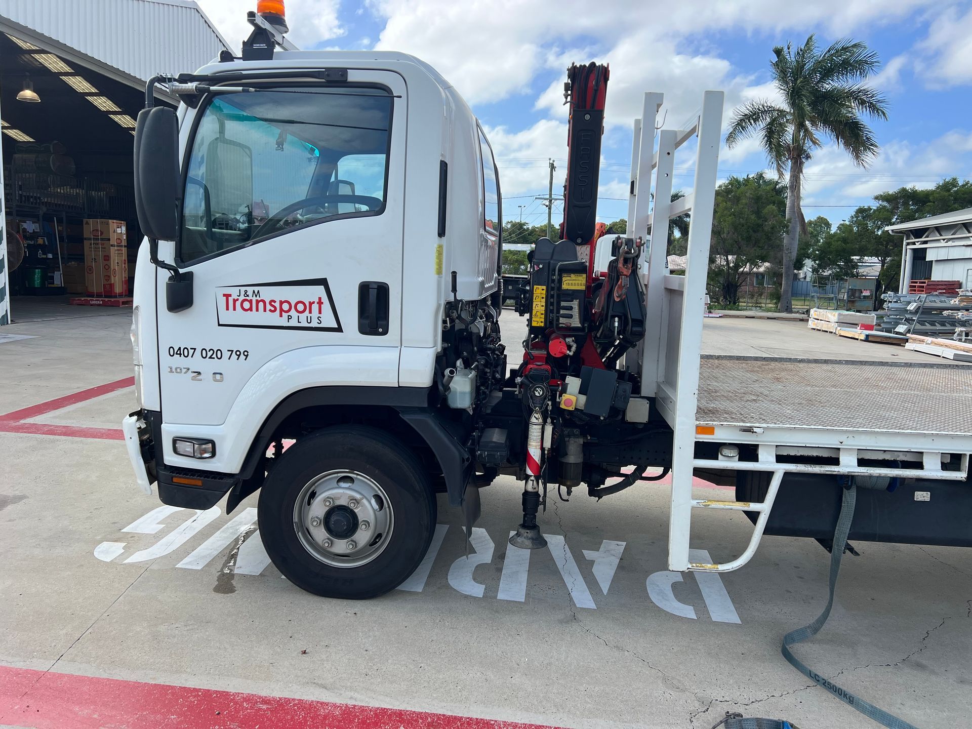 White flatbed truck parked at a loading bay, with a crane mounted behind the cab.