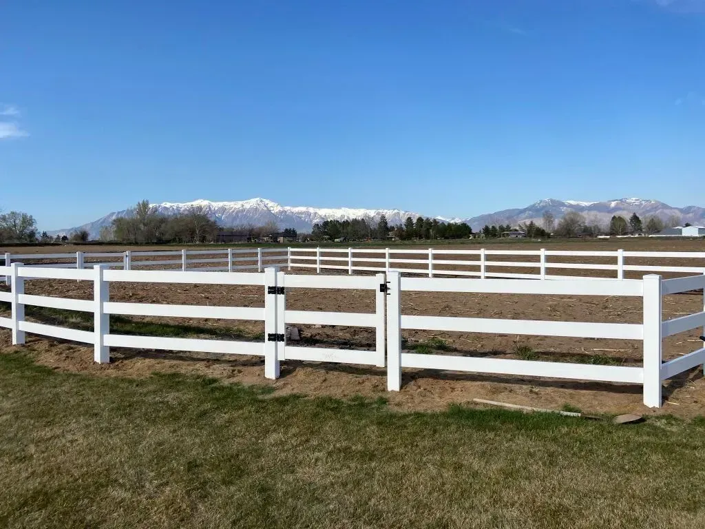 White fenced paddock with green grass and snow-capped mountains under a clear blue sky
