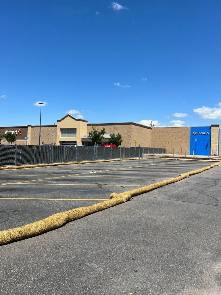 Empty parking lot beside a tan building under a blue sky, with a yellow hose or barrier across the pavement