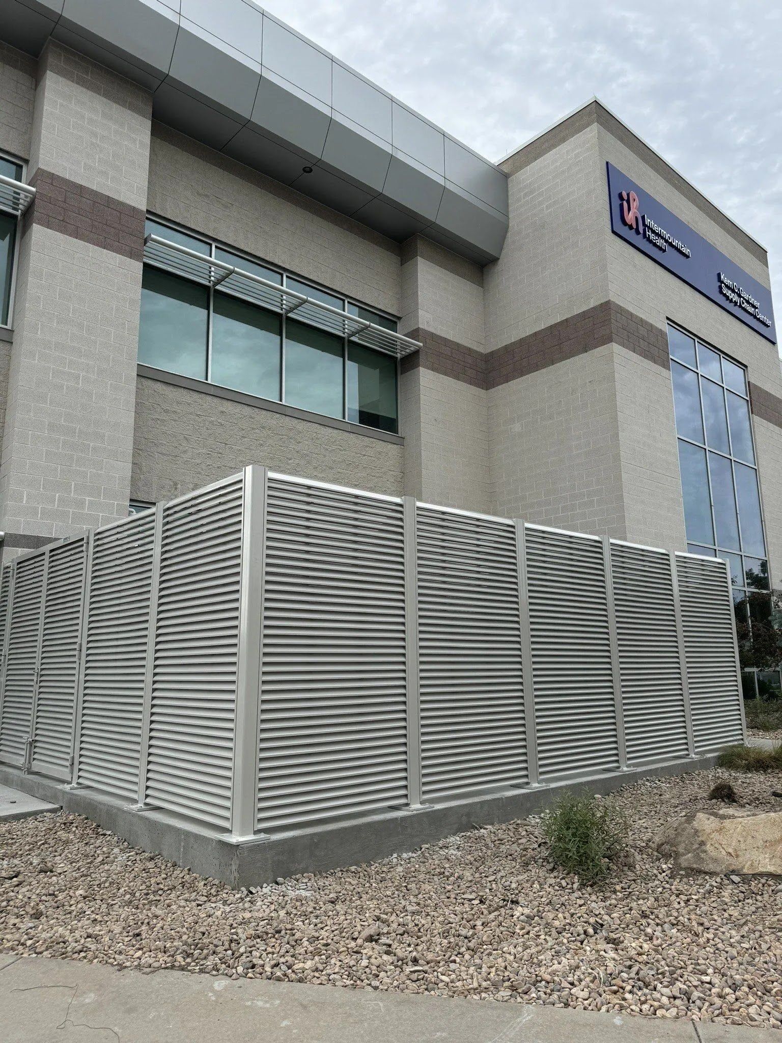 Modern commercial building exterior with a white slatted fence and gravel landscaping