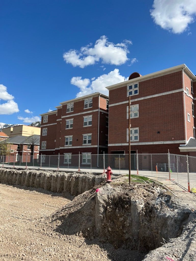 Brick apartment buildings beside a large excavation site under a blue sky with clouds