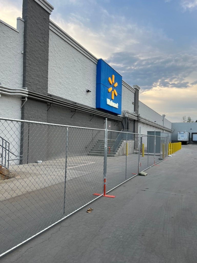Chain-link fencing blocks a storefront with a blue sign on a quiet paved street at dusk.
