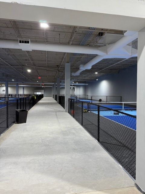 Indoor sports facility with elevated walkway beside blue courts and chain-link fencing