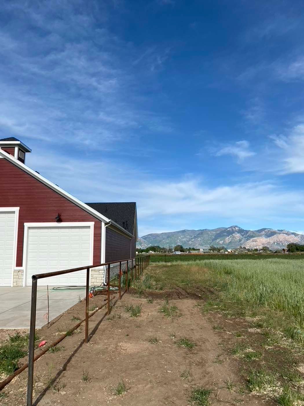 Red barn beside a dirt path, with green field and mountains under a blue sky.