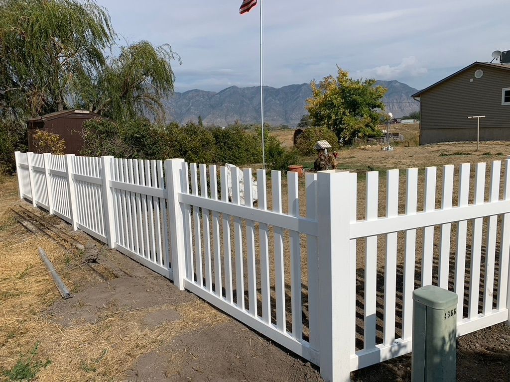 White picket fence along gravel driveway with mountains in the background
