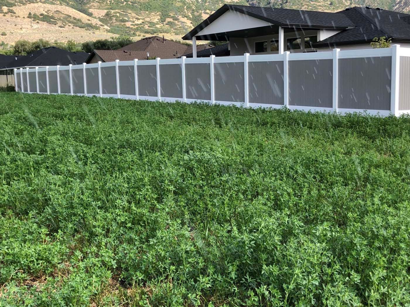 White fence beside a lush green field with a house and hillside in the background