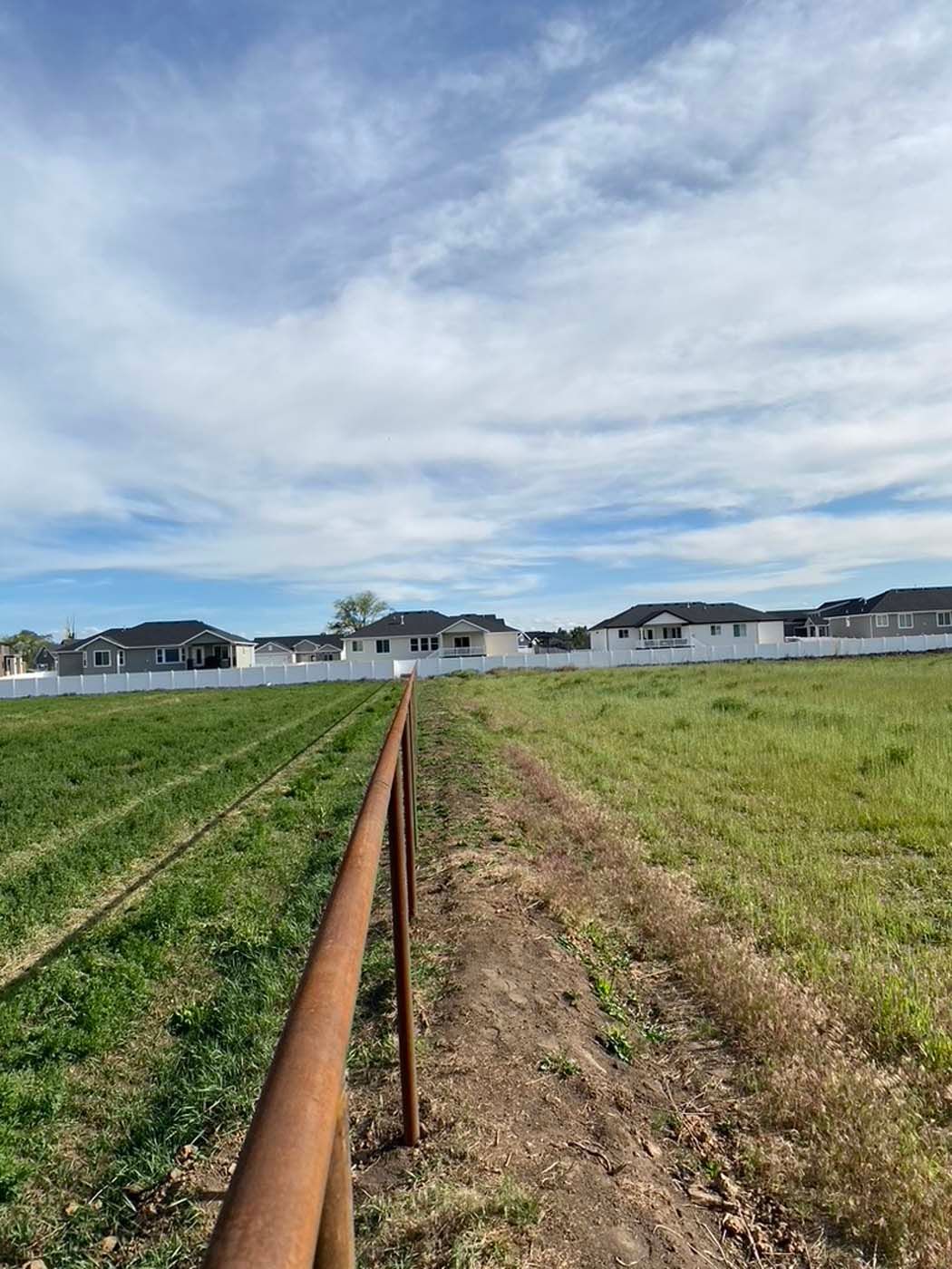 Rusty irrigation pipe running through a grassy field toward white houses under a cloudy sky