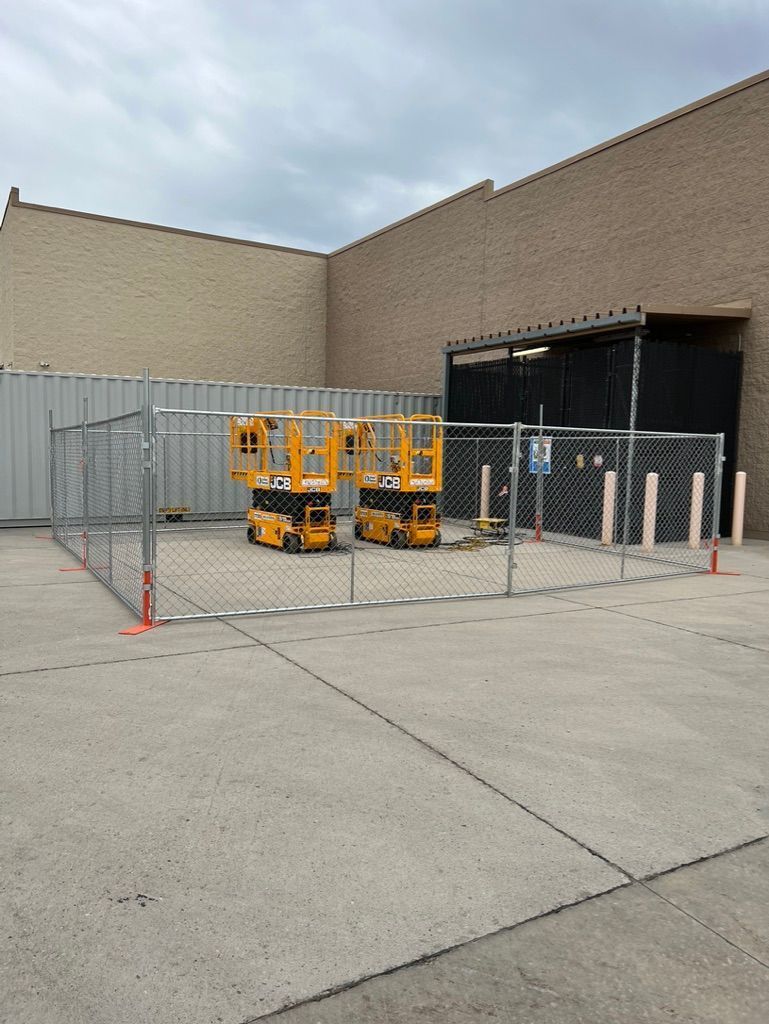 Empty concrete loading area with fenced-off yellow scissor lifts beside a brick building