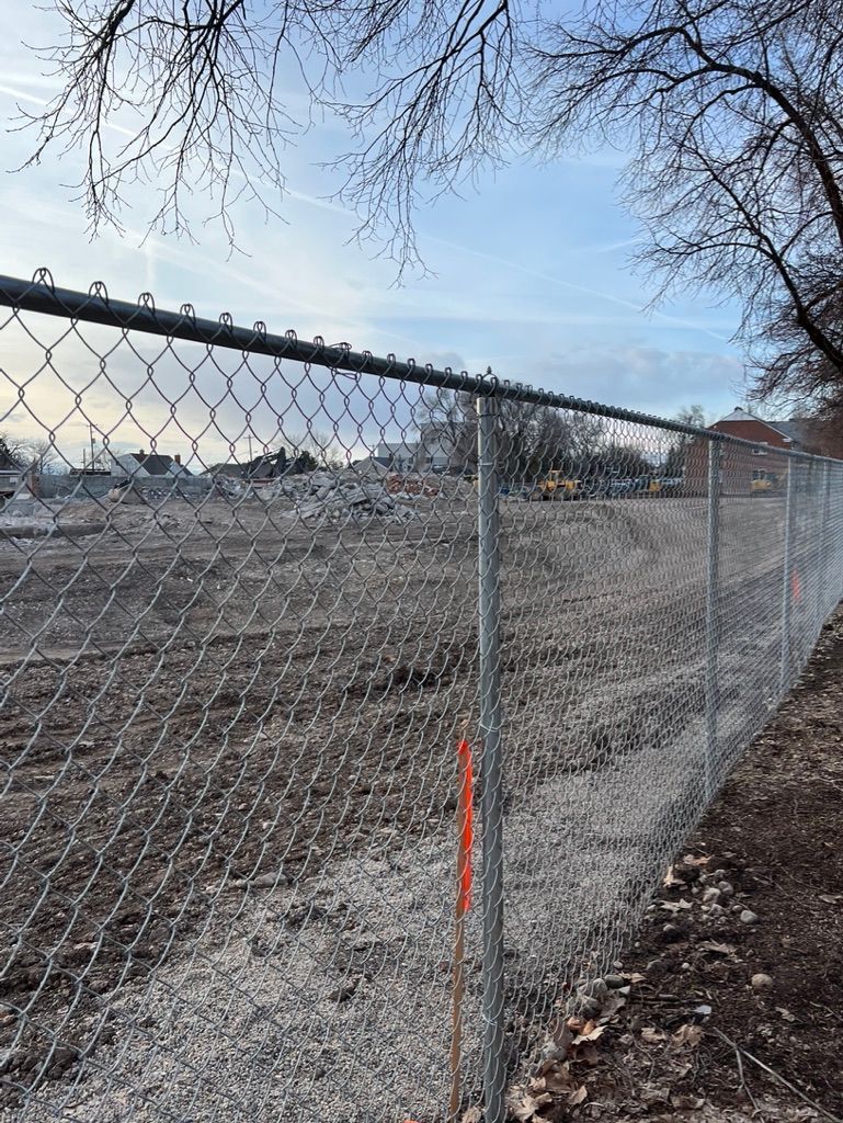 Chain-link fence beside a muddy construction site under a cloudy sky.