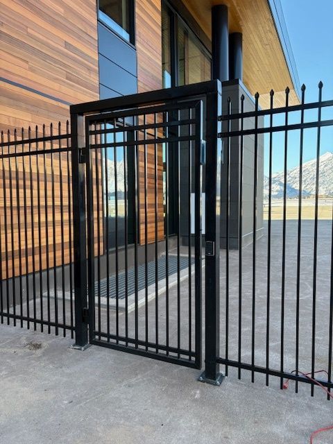 Black metal gate beside a modern wooden building and concrete walkway