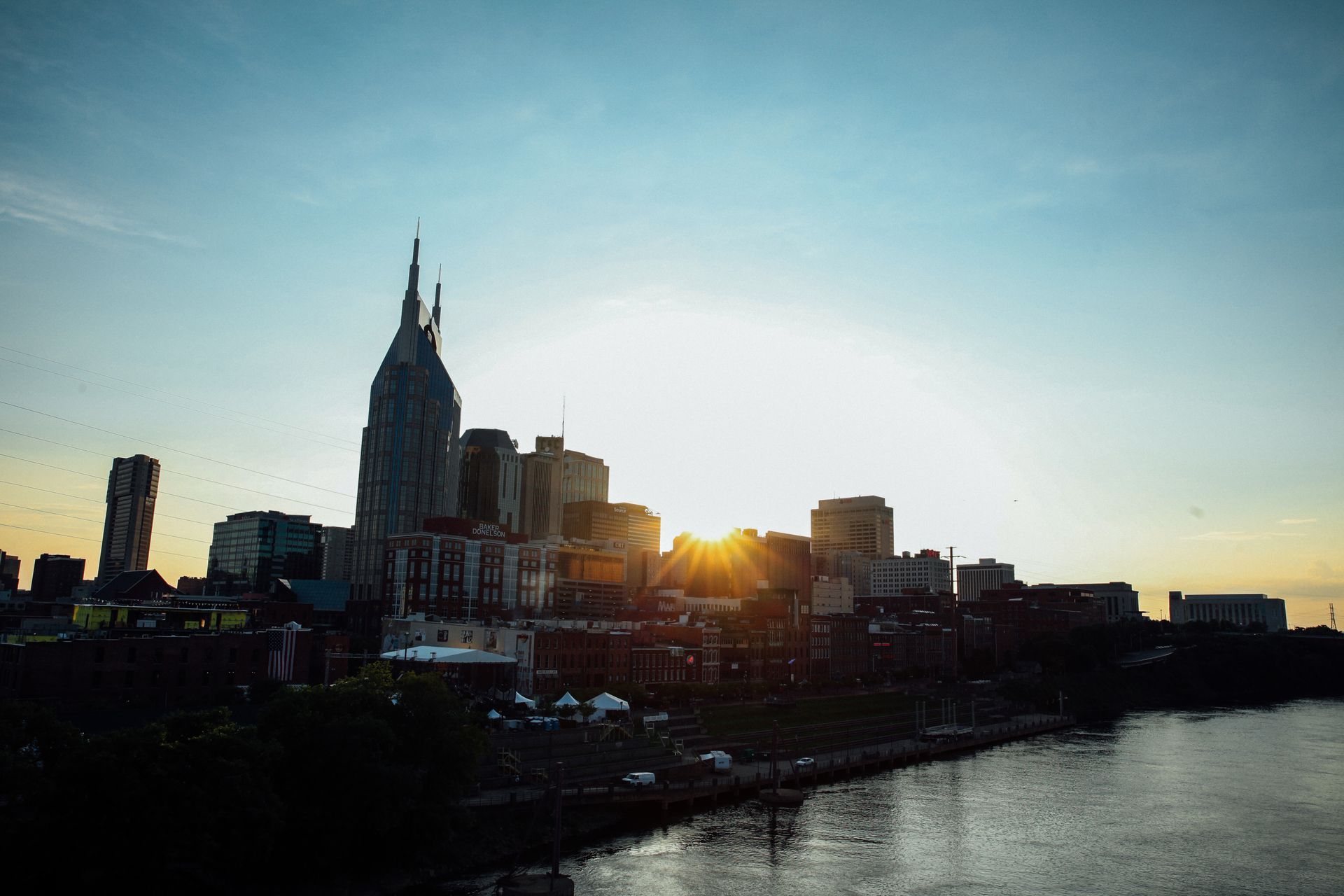Sunset skyline over a river, with silhouetted buildings and a tall spired tower.