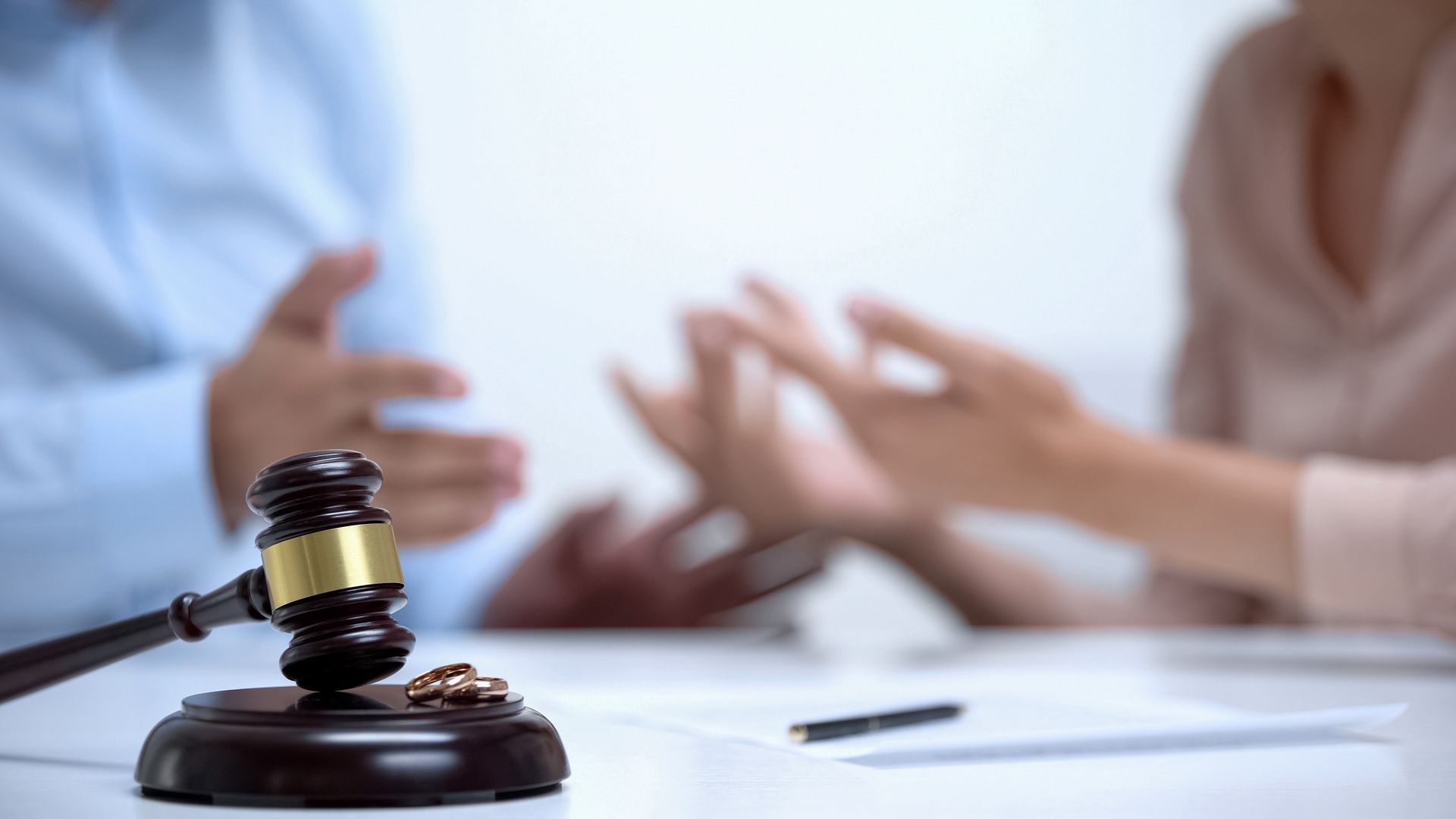 Spouses arguing about property division during divorce, gavel and rings close-up.