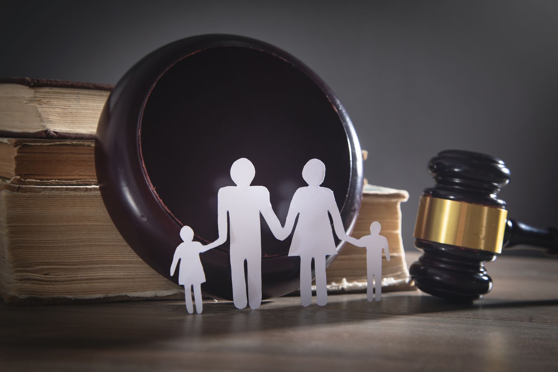 Close-up of family paper silhouette against a wooden gavel and scale, representing family law Family silhouette figures before a law book and judge’s gavel on a table