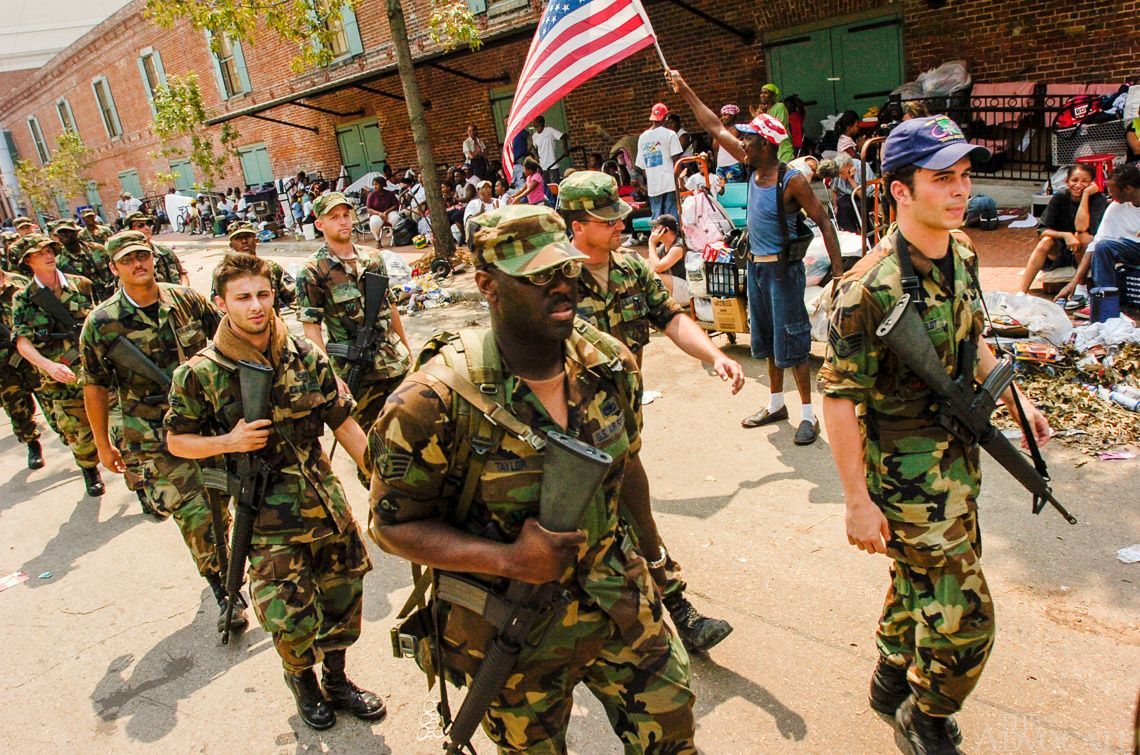 A group of soldiers marching down a street holding an american flag