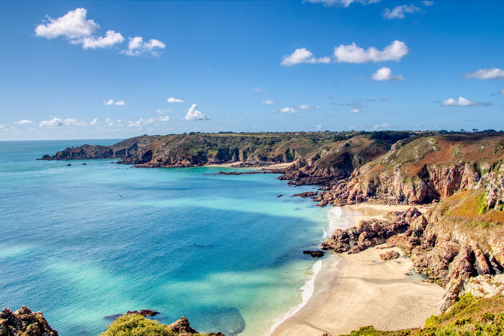 Scenic coastal view: turquoise water, sandy beach, rocky cliffs, and bright blue sky.