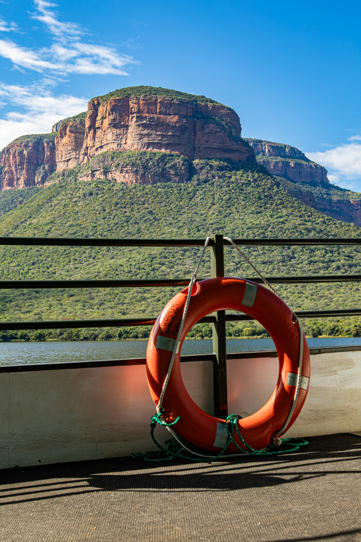 Orange life preserver on a boat, with a mountain and green trees in the background under a blue sky.