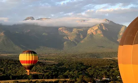 A hot air balloon is flying over a valley with mountains in the background.