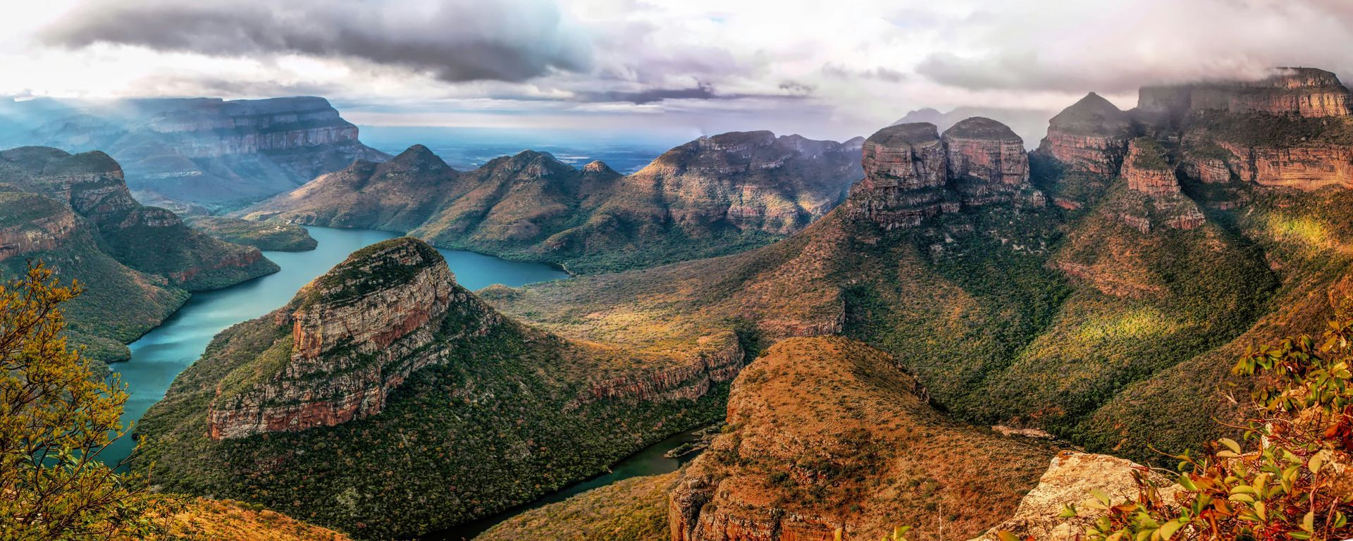 A panoramic view of a river surrounded by mountains and trees.