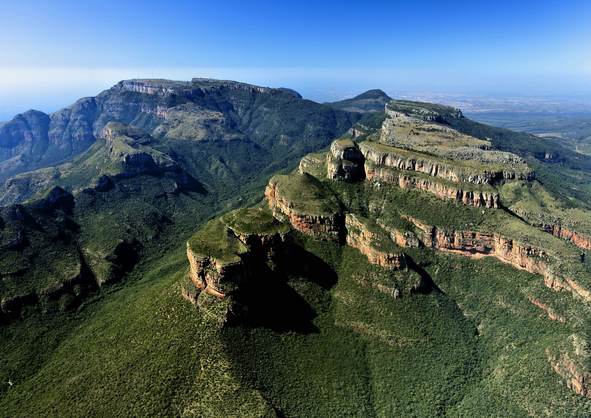 an aerial view of a lush green mountain range with a blue sky in the background .