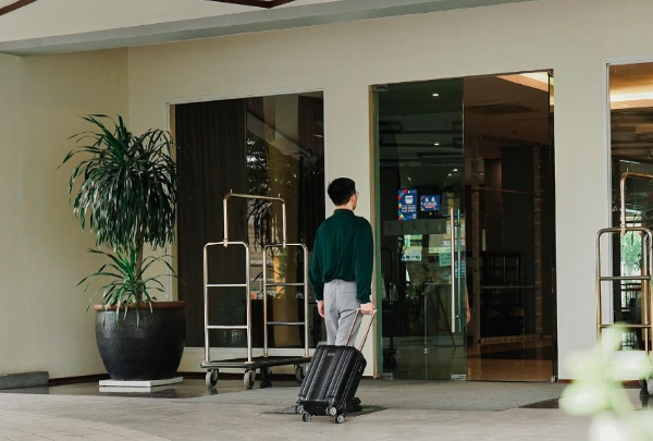 Person with rolling suitcase entering a building through glass doors.