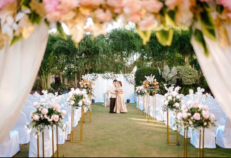 Wedding ceremony with floral arch, aisle with flower stands, couple embracing in front of floral backdrop, outdoors.