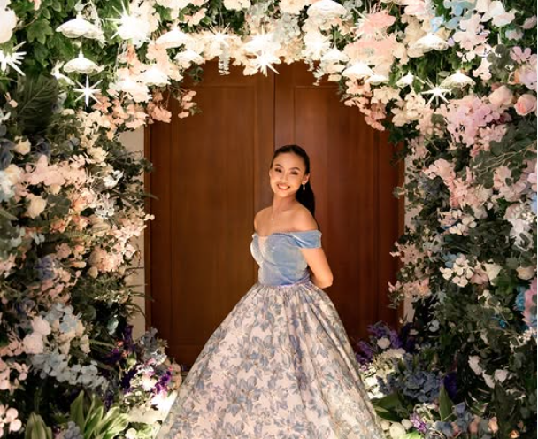 Woman in ball gown poses in front of floral archway.