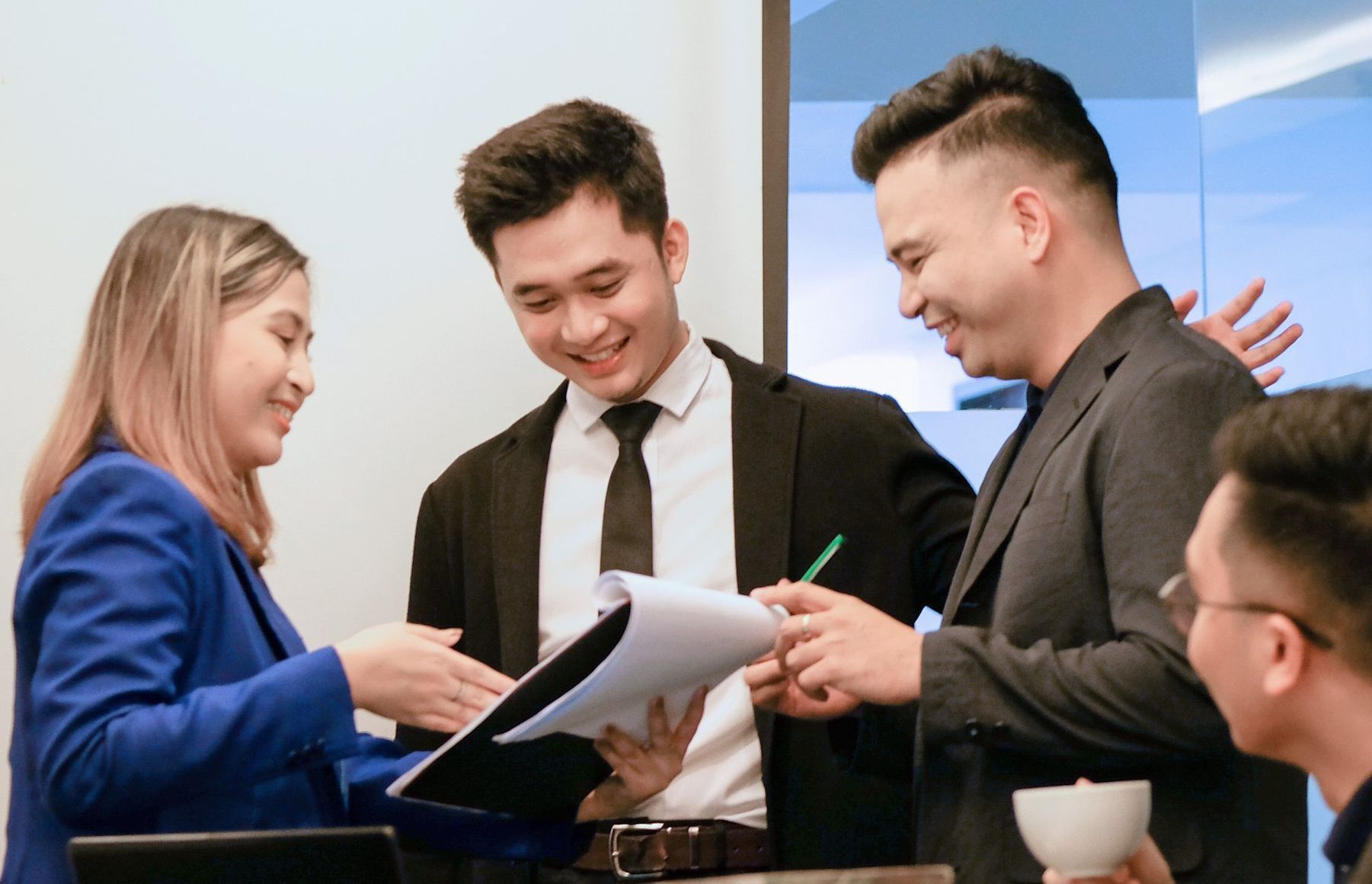 Four colleagues in professional attire collaborate over a document during a discussion in a bright office space.