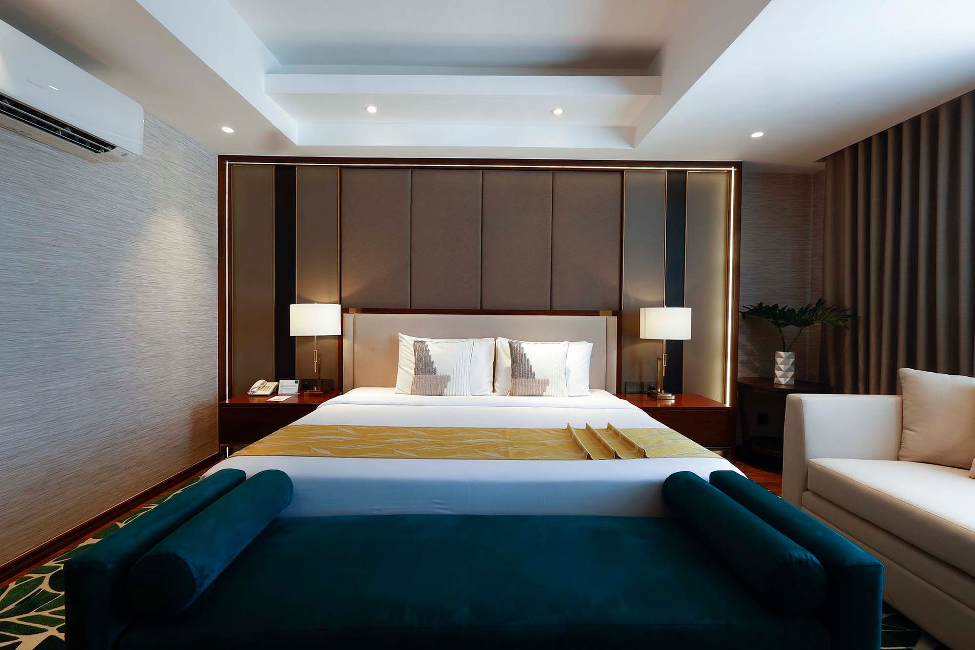 Hotel room with king-size bed, sofa, side tables, and decorative wall paneling.