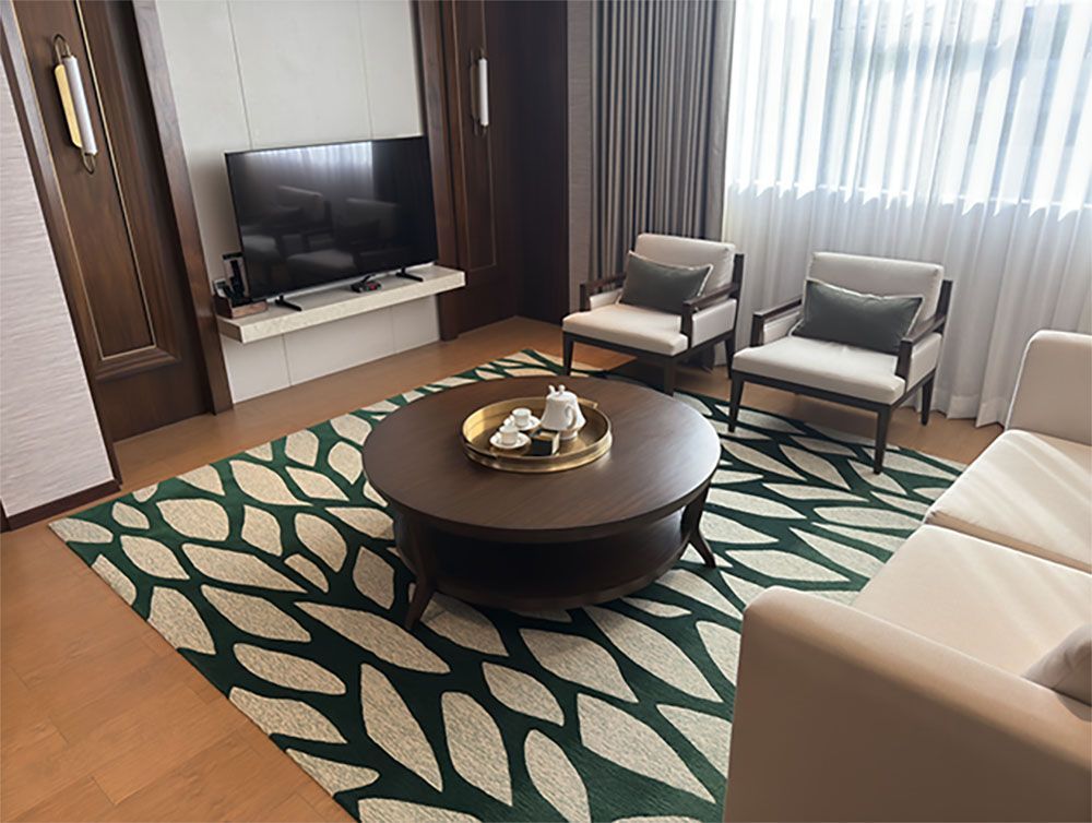 Living room with green and cream leaf-patterned rug, two armchairs, a couch, a round coffee table, and a TV.
