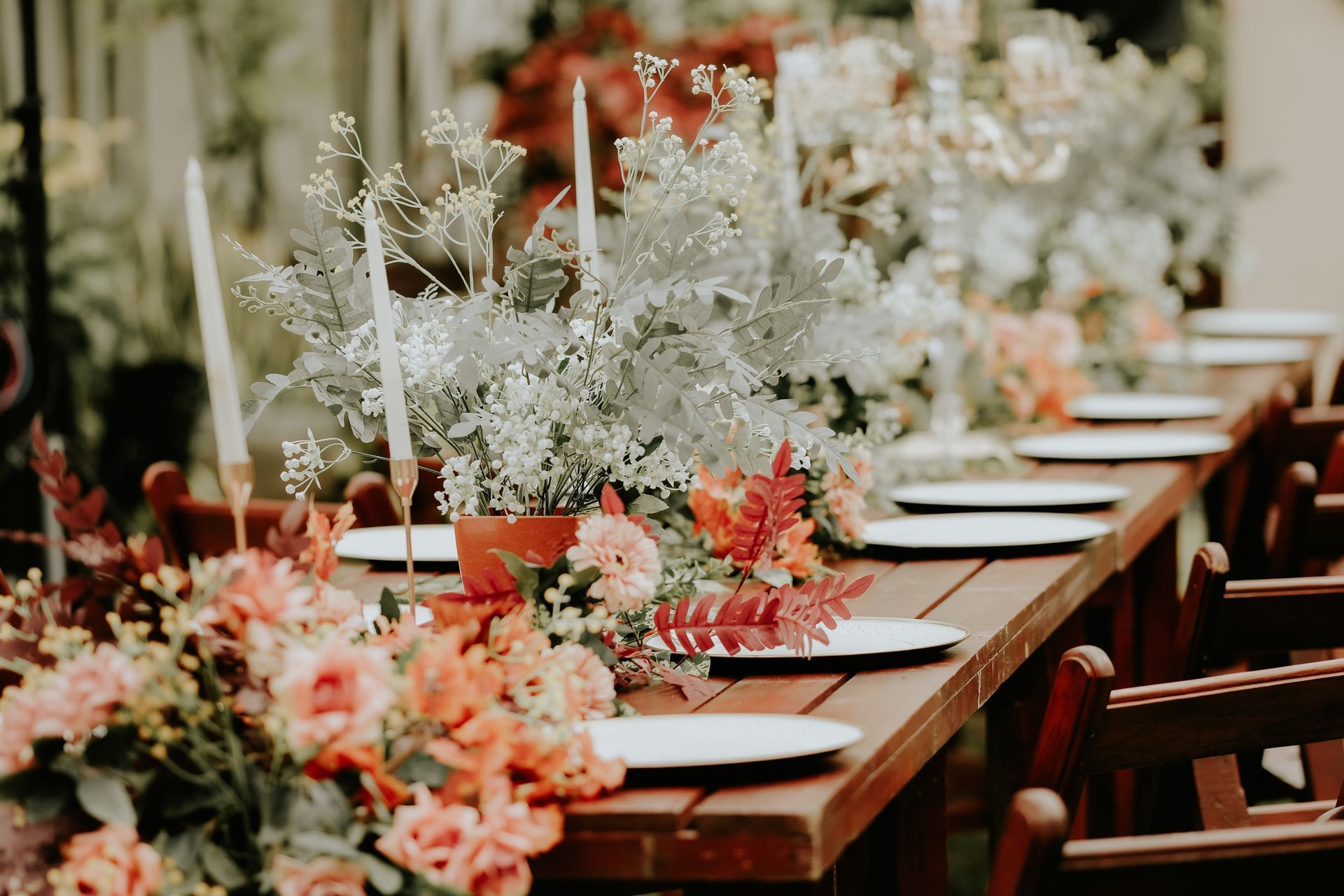 Elegant outdoor dining table with white plates, coral floral arrangements, and greenery-lined place settings