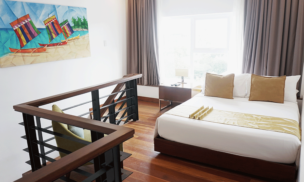 Loft bedroom with wooden floors, bed with gold accents, artwork, and stair railing.
