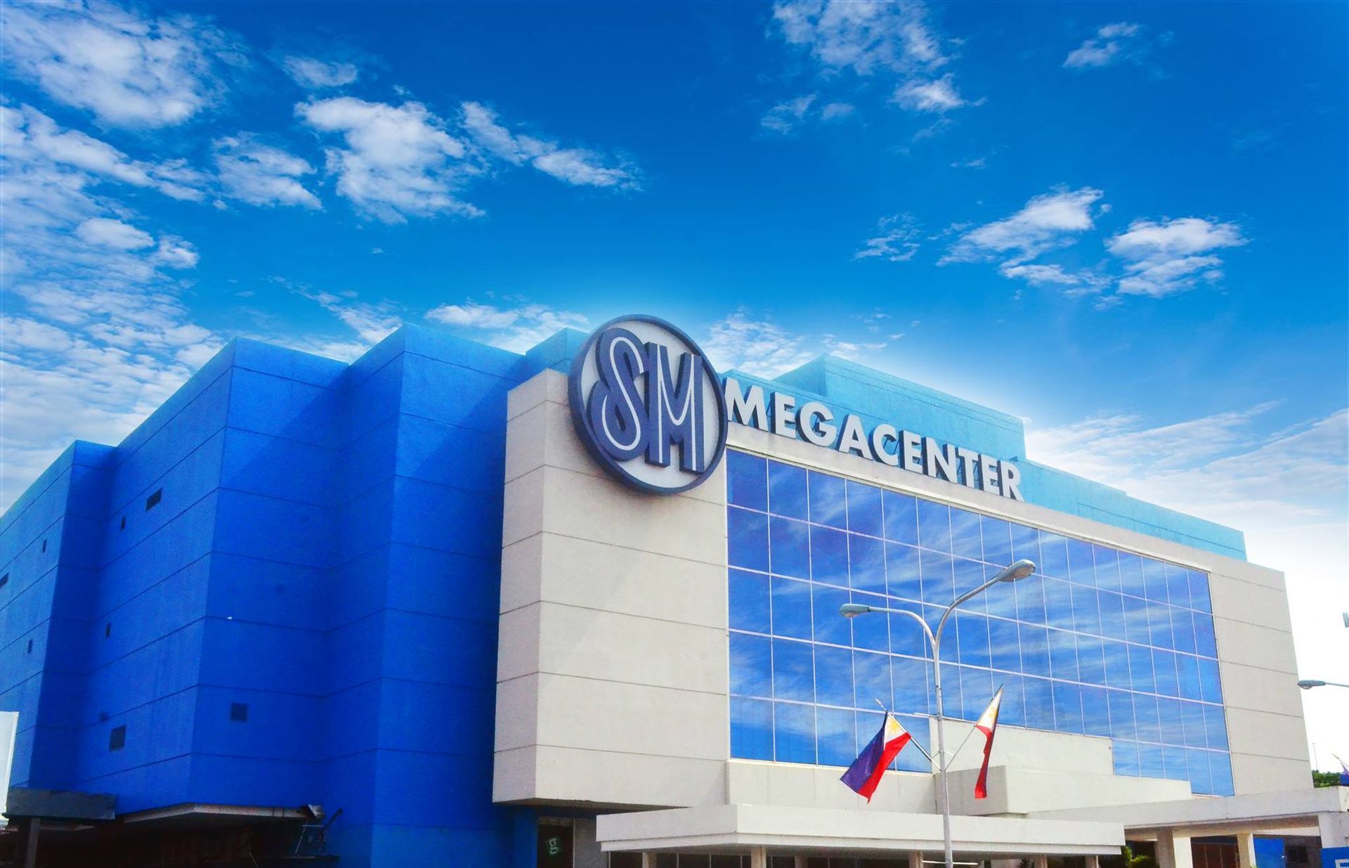 SM Megacenter building with blue exterior and logo against a blue sky with flags.
