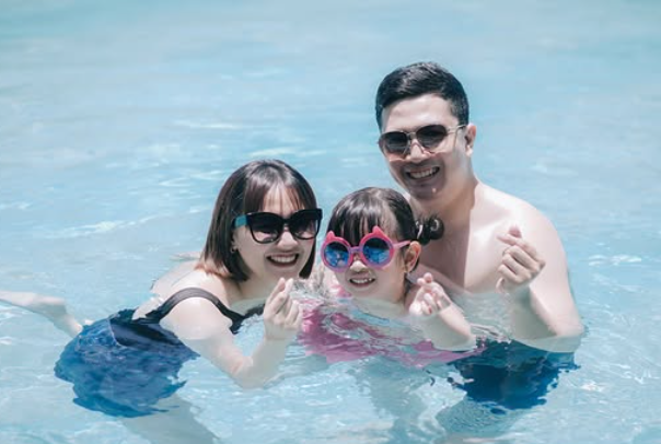 Three people smiling in a swimming pool, wearing sunglasses and enjoying the water