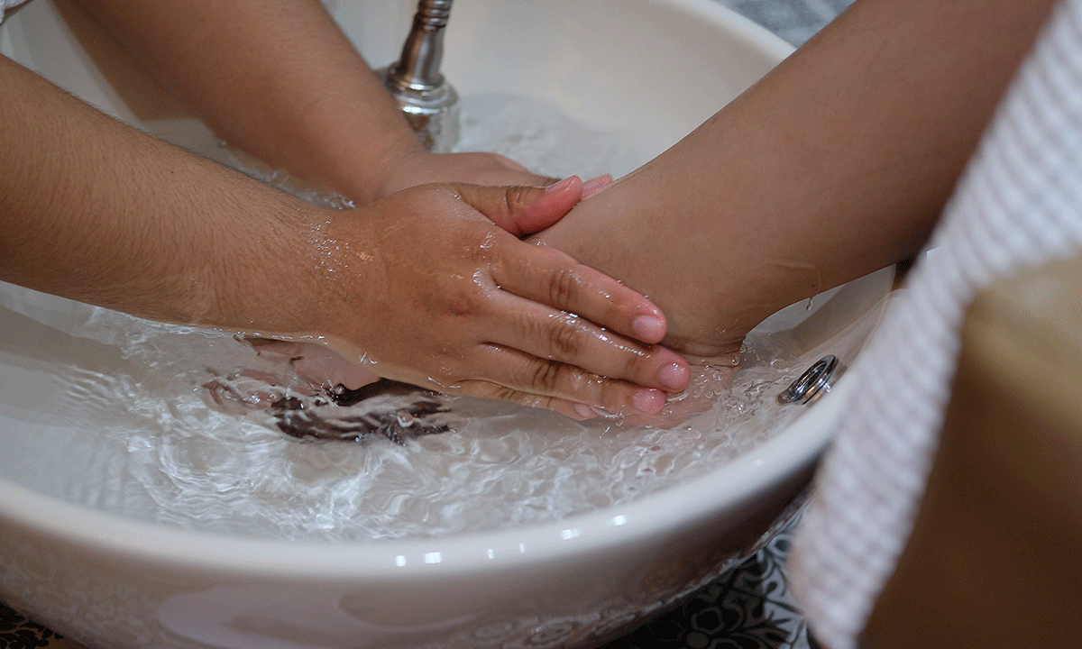 Hands soaking a foot in a white basin of water, possibly a pedicure.