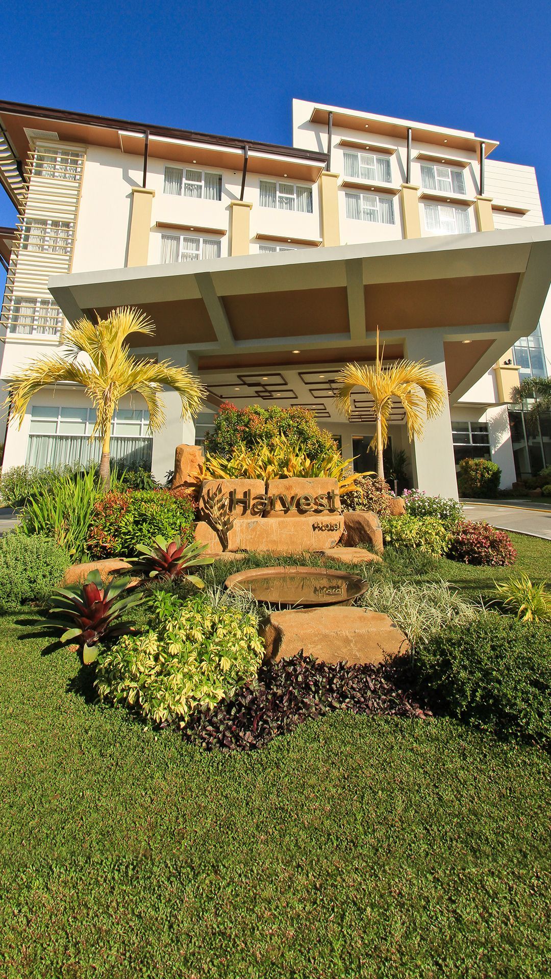 Harvest Hotel exterior with lush gardens and palm trees in Cabanatuan City