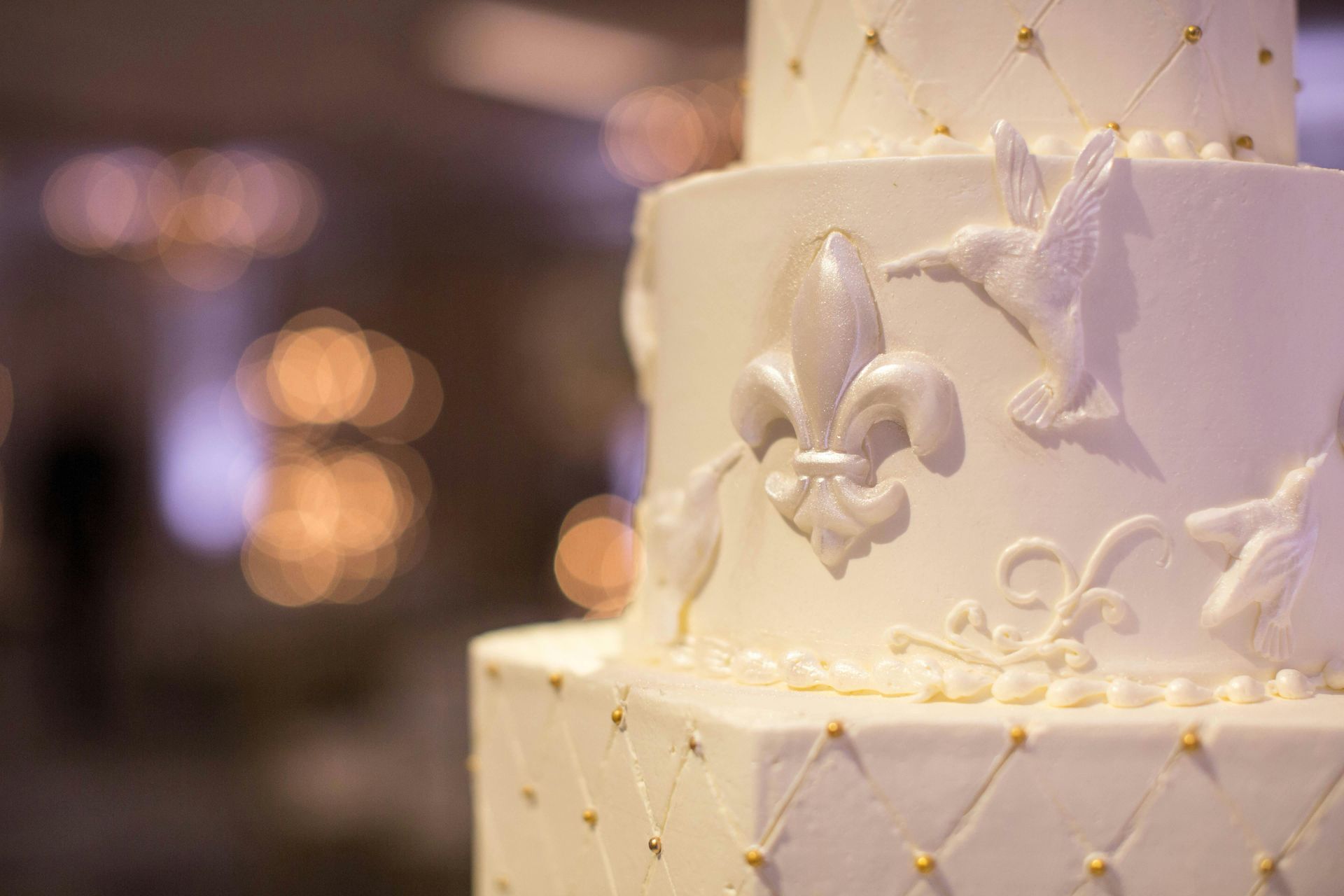 White tiered wedding cake decorated with fleur-de-lis and gold accents.