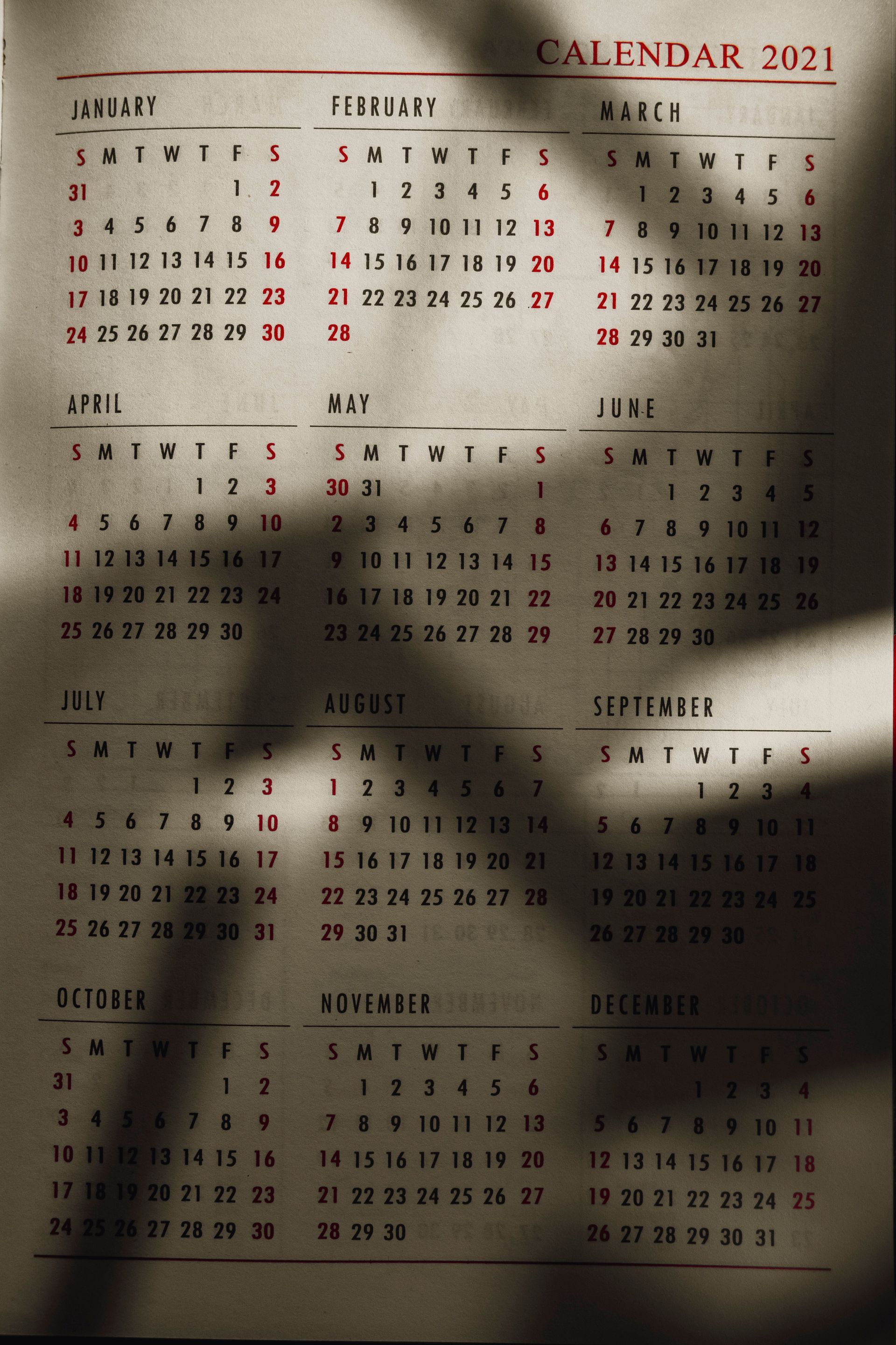 2021 wall calendar with months in black and red, partly shadowed by sunlight