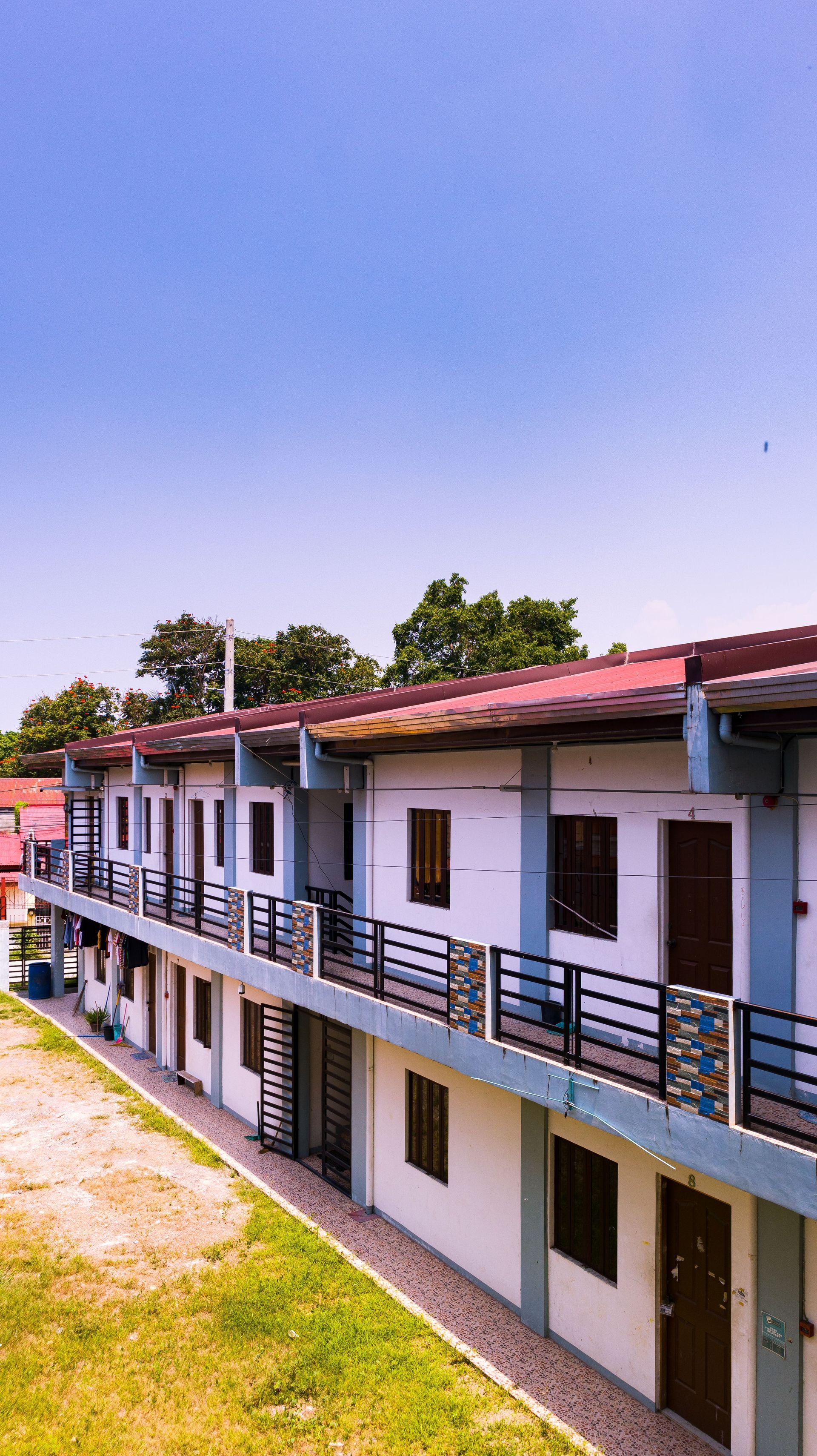 Two-story white building with red roof and black railings beside a walkway under a clear blue sky